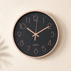 Black wall clock with rose gold numerals and rim on a warm beige background