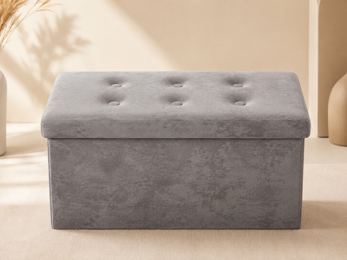 Grey velvet storage bench with tufted lid on a warm beige background