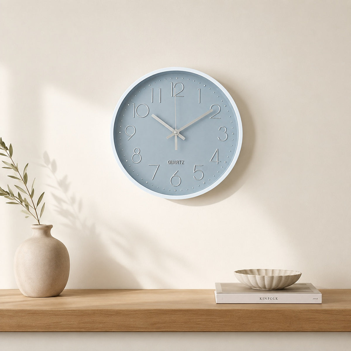 Grey and silver wall clock above a light wooden shelf in a calm beige interior