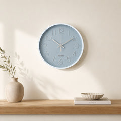 Grey and silver wall clock above a light wooden shelf in a calm beige interior