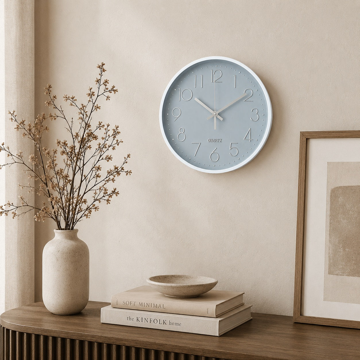 Modern grey wall clock with silver details displayed above a wooden sideboard