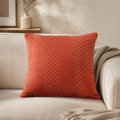 Terracotta chevron cushion styled on a beige armchair in a cosy reading corner