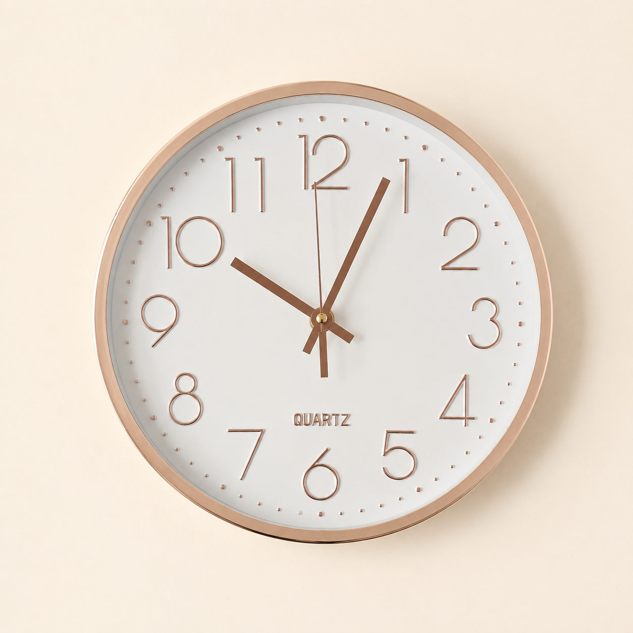 White wall clock with glossy rose gold details on a warm beige background