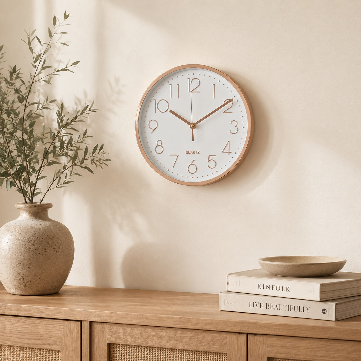 Rose gold and white wall clock above a wooden cabinet with minimalist decor